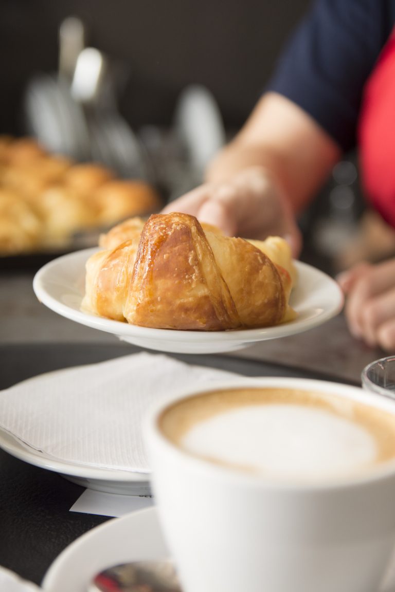 primer plano de la mano de la camarera ofreciendo croissant al horno